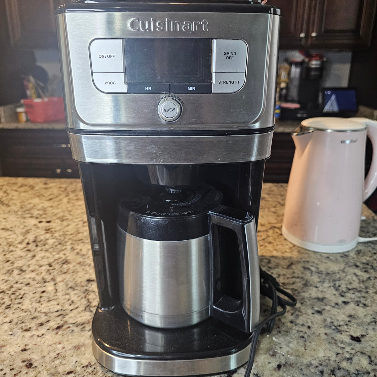 Silver coffee maker with digital display on granite counter, pink electric kettle beside it.