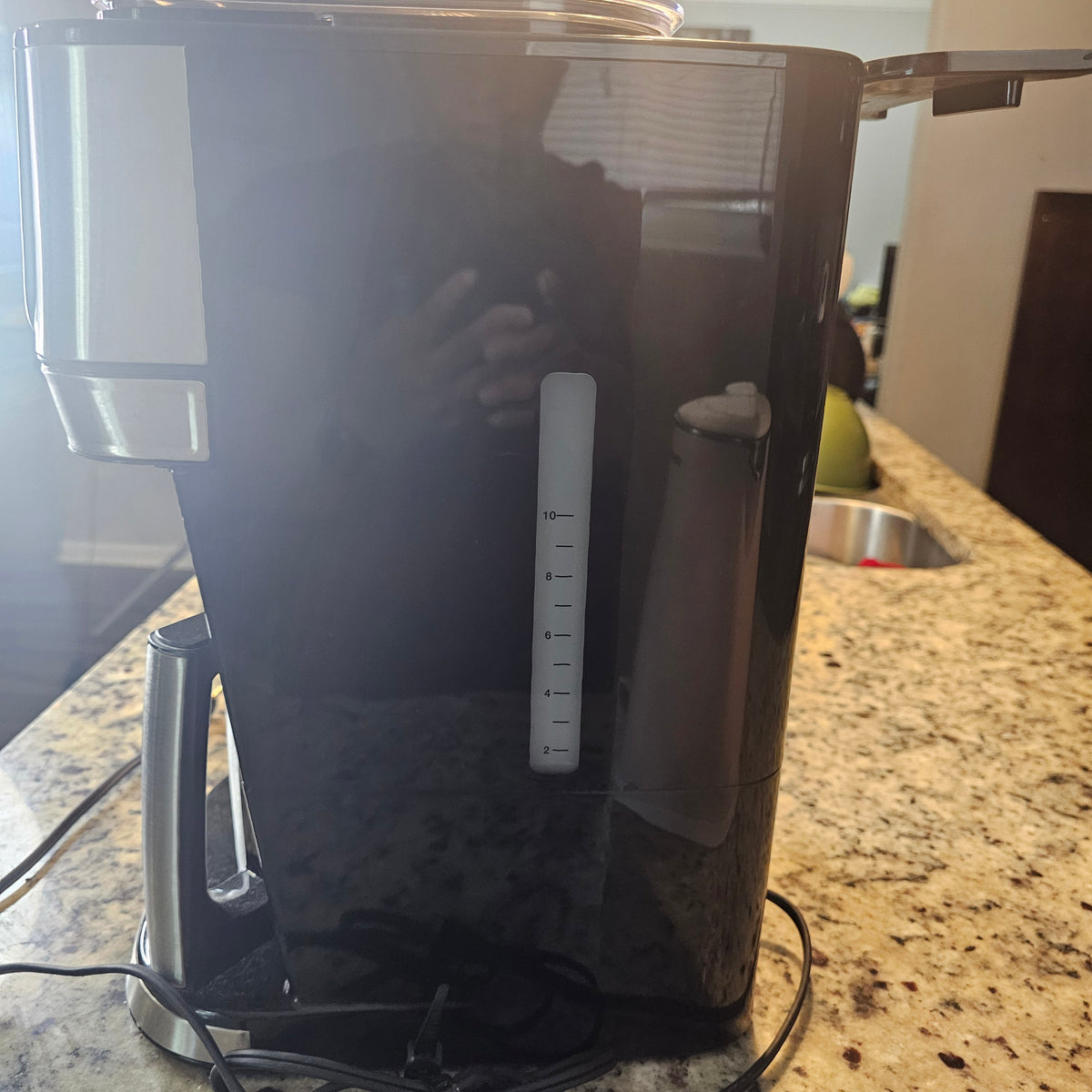 Black coffee maker on a granite countertop with a water level indicator and a reflection.