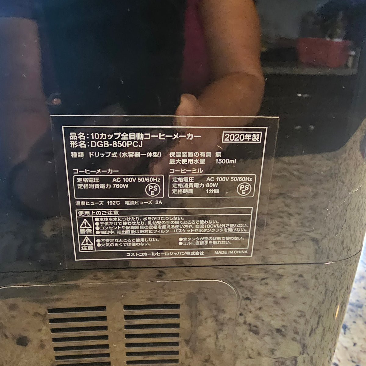 Close-up of a black device with a label showing text in Japanese, reflecting a person.