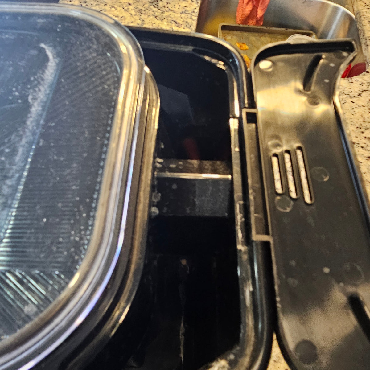 Open black plastic container with a lid, placed on a speckled countertop.