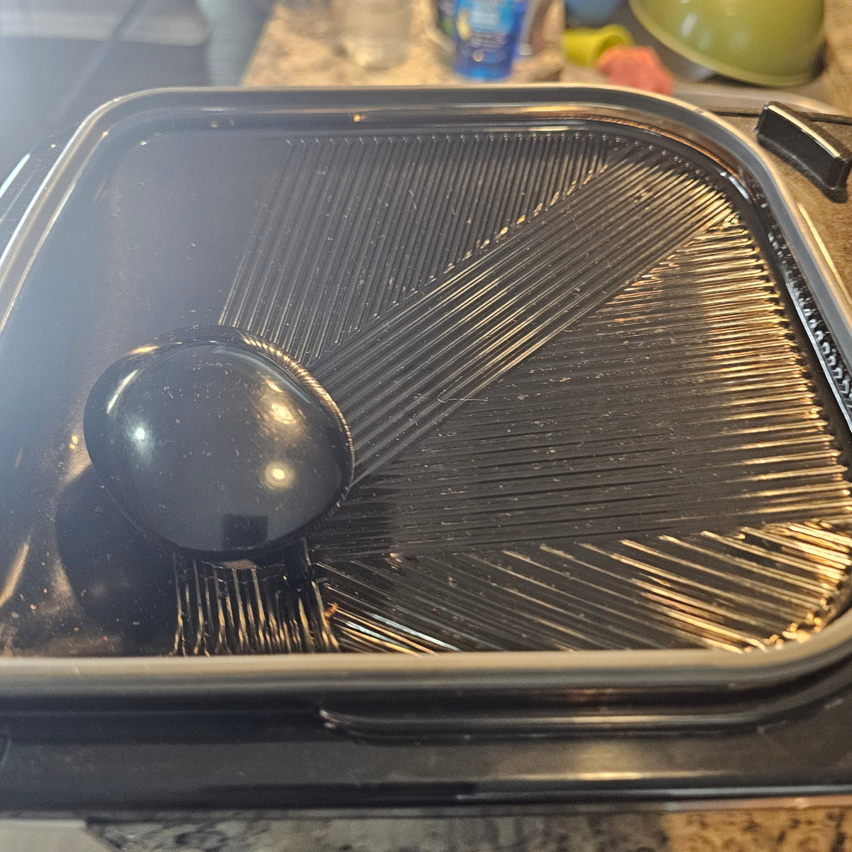 Black ribbed pan with a round handle, glossy finish, resting on a kitchen countertop.