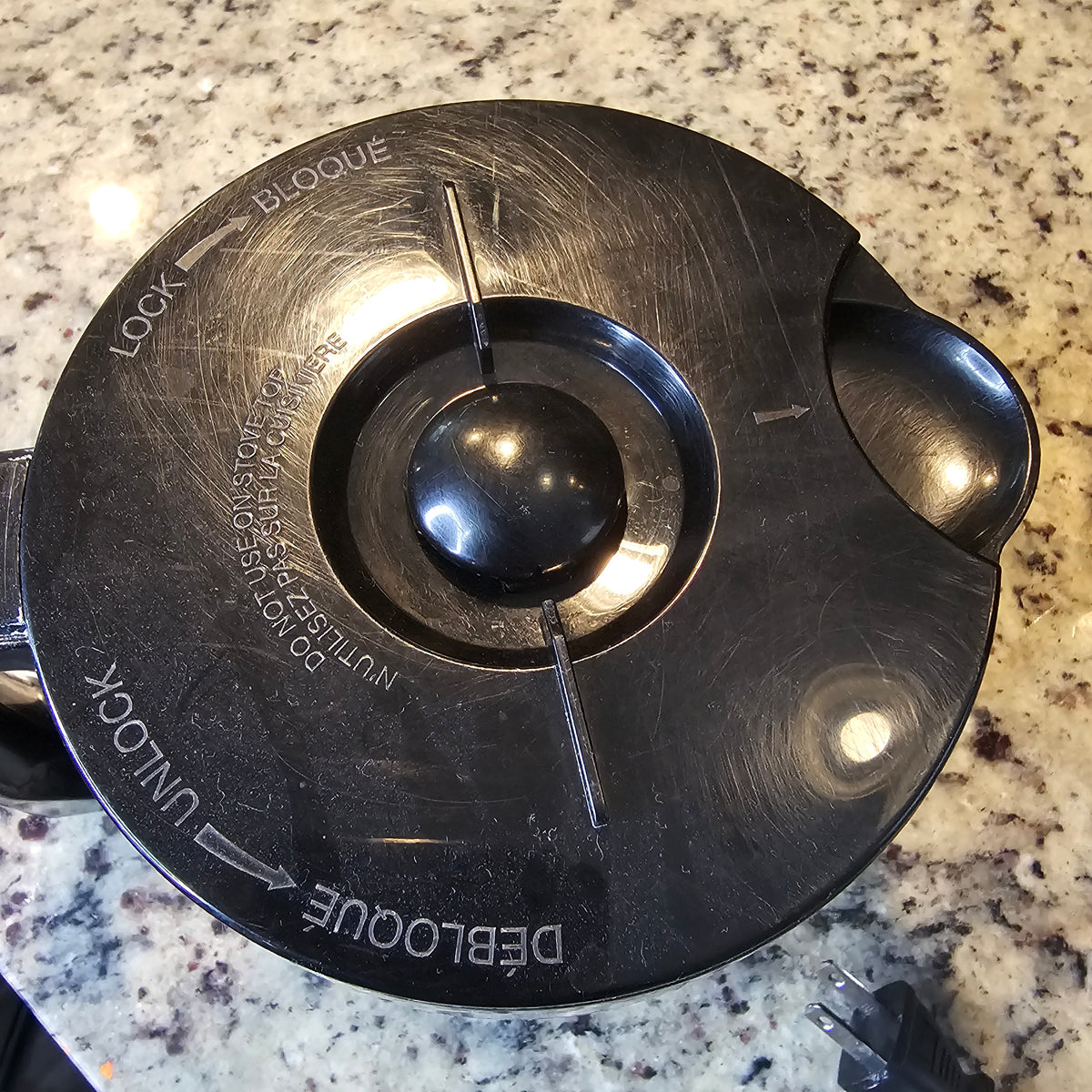 Black circular lid with lock/unlock text, placed on a speckled granite countertop.