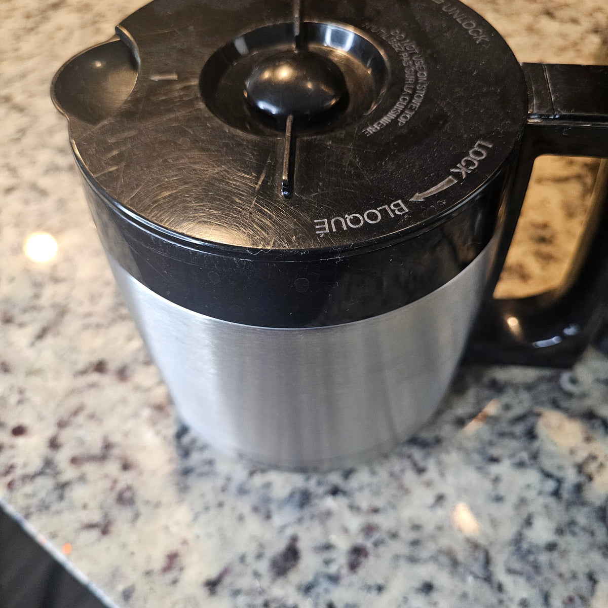Stainless steel pot with black lid and handle on speckled granite countertop.