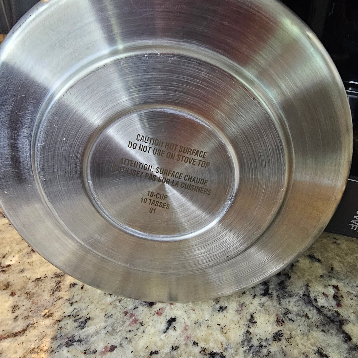Stainless steel pot bottom with engraved text on a speckled granite countertop.