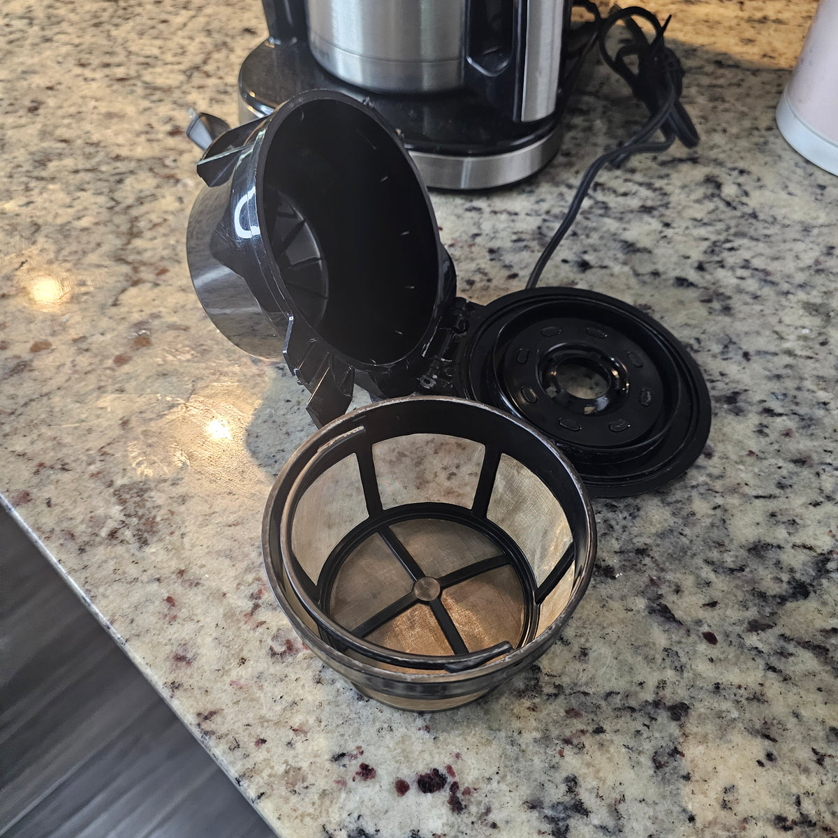 Coffee maker with open lid and mesh filter on granite countertop.