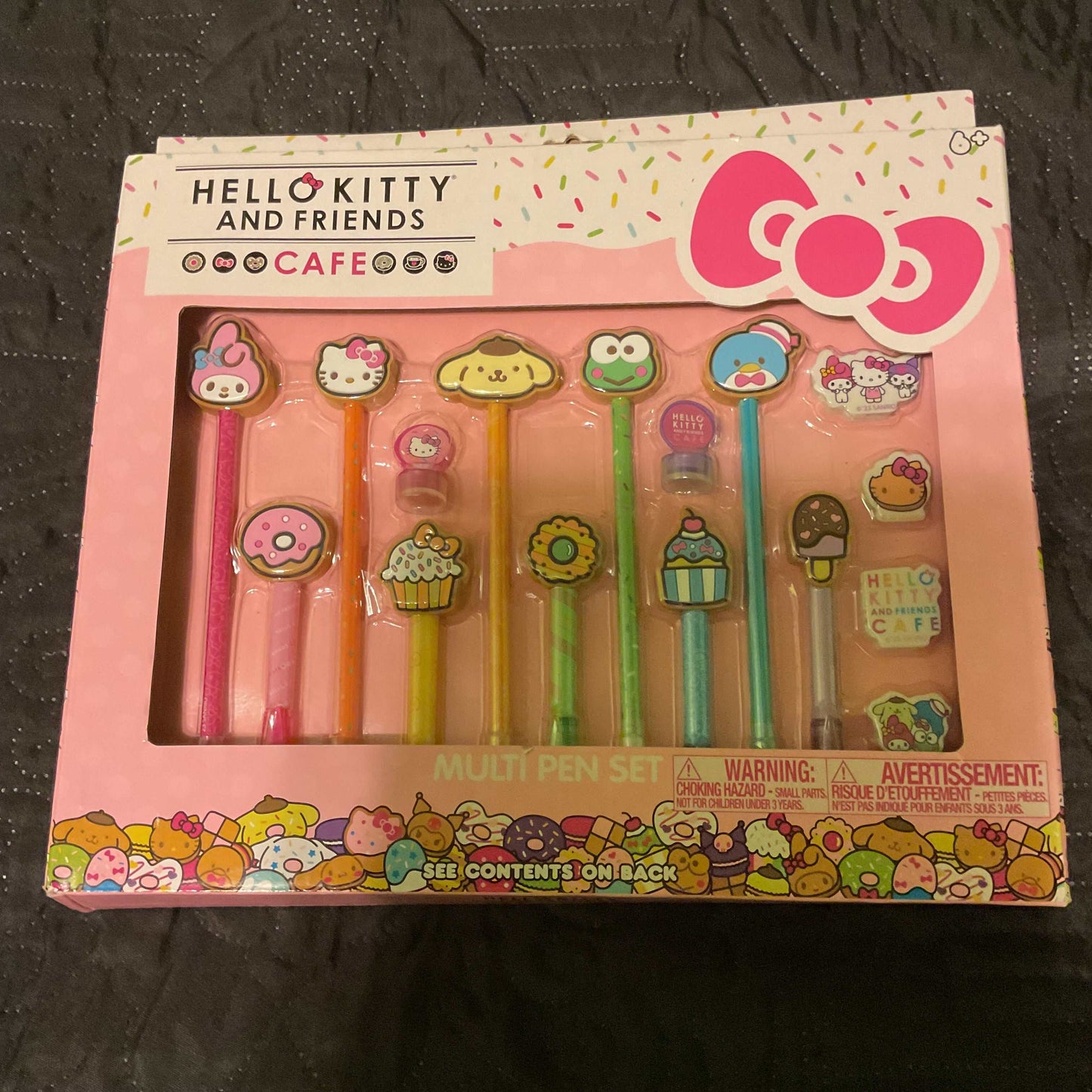 Hello Kitty & Friends Cafe multi-pen set with 10 colorful ballpoint pens featuring character and treat-themed toppers, bonus rubber toppers, erasers, and stamps in pink packaging.