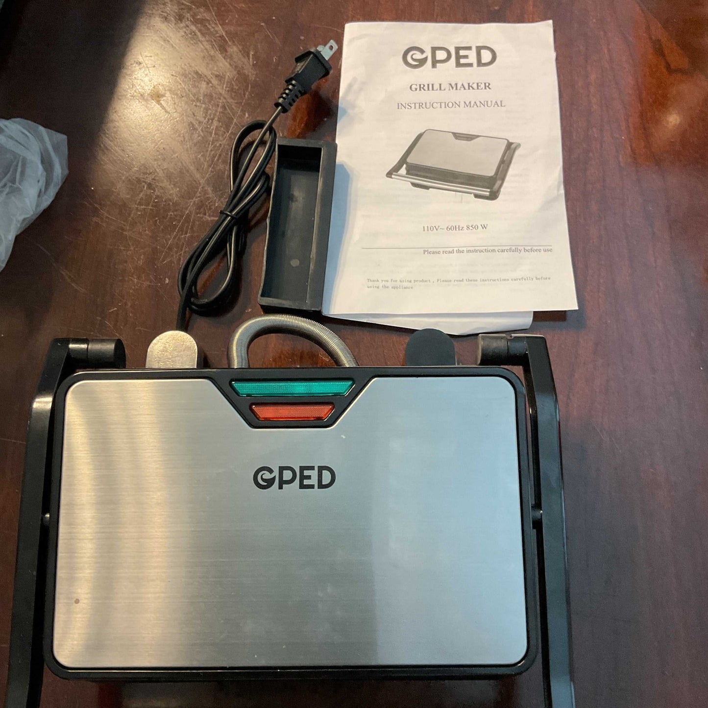 GPED 850W Electric Grill & Sandwich Maker with stainless steel top, power cord, and instruction manual on wooden surface