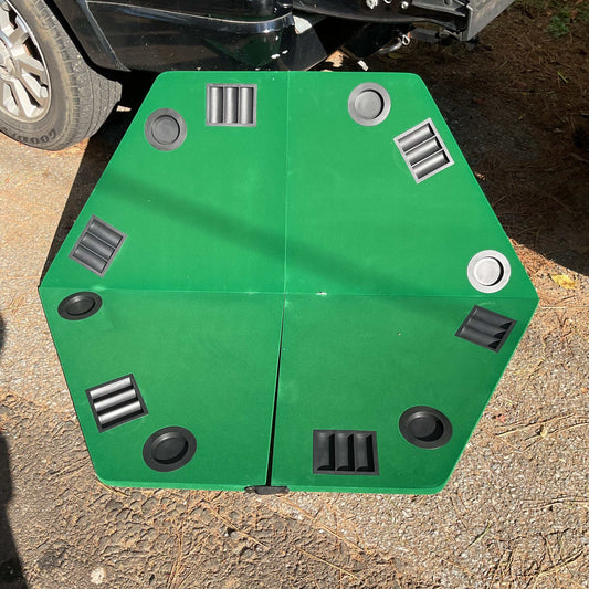 Folding poker table top with green felt, six player chip trays, and drink holders on outdoor ground near vehicle